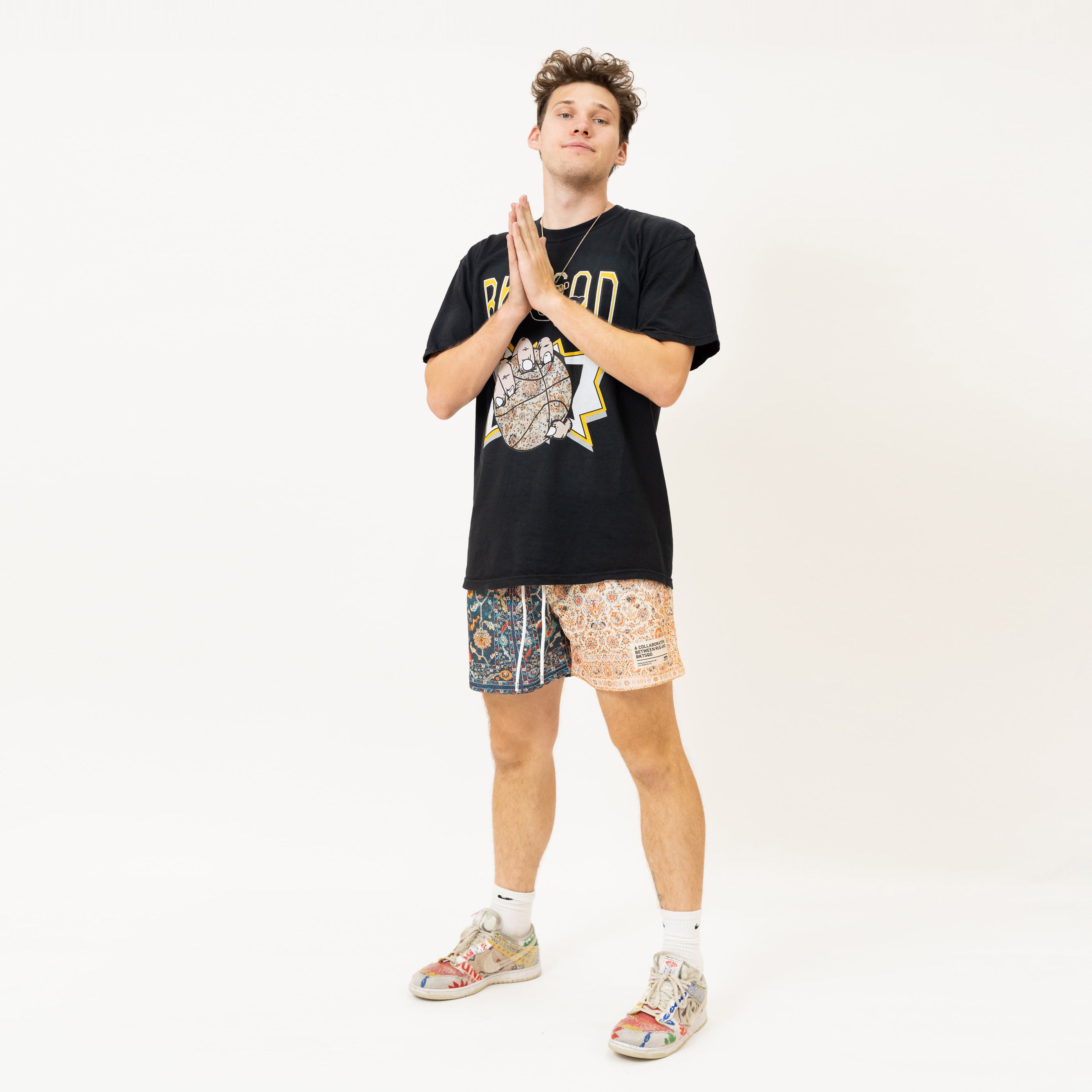 Jesse Riedel known as Jesser wearing the black bucketsquad collab shirt with faze rug. Paired with the two tone basketball shorts, Jesse stands with his hands in a prayer pose with a white background. 